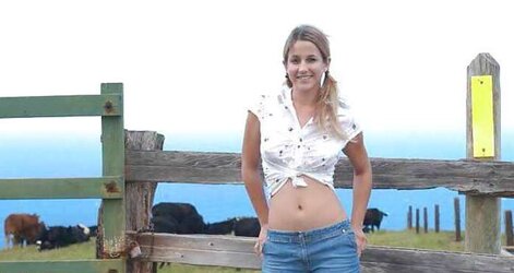 Blonde teenager unclothes infront of a fence for cows